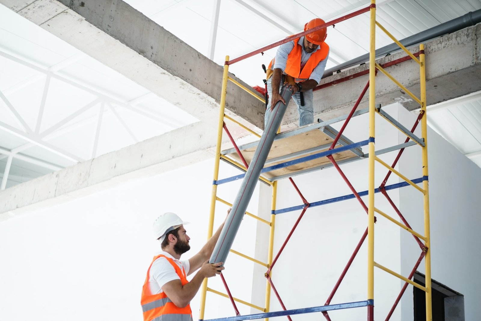 Two men builder in uniform drag the pipe on scaffolding at construction site