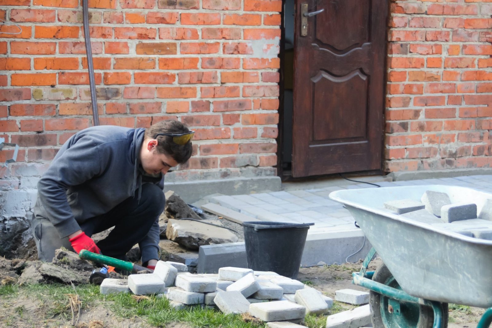 Man digging. Defocus young man laying gray concrete paving slabs in house courtyard on gravel founda